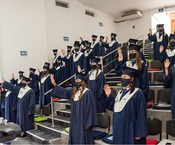 Grados 2021-1 UNIMINUTO Pereira Estudiantes de píe usando toga azul con la mano derecha levantada haciendo juramento de grado