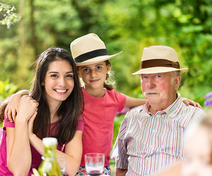 Red de familias con sentido Tres personas reunidas en una foto familiar donde está un señor mayor, una mujer y una niña. Un fondo con naturaleza de color verde