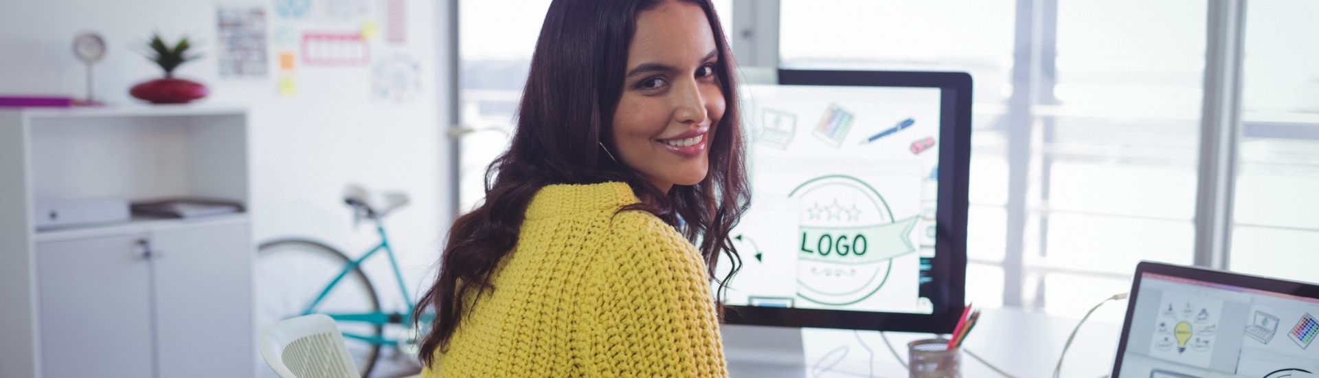 Mujer sentada frente a un computador, voltea sonriente para mirar a la cámara