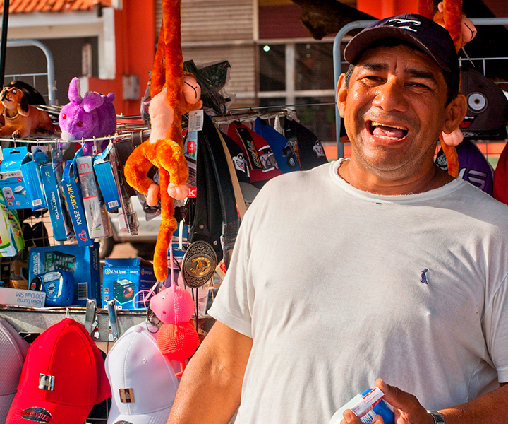 UNIMINUTO acompañando la reactivación económica en Pereira Vendedor informal sonriendo, al fondo se ve su puesto de trabajo con los productos.