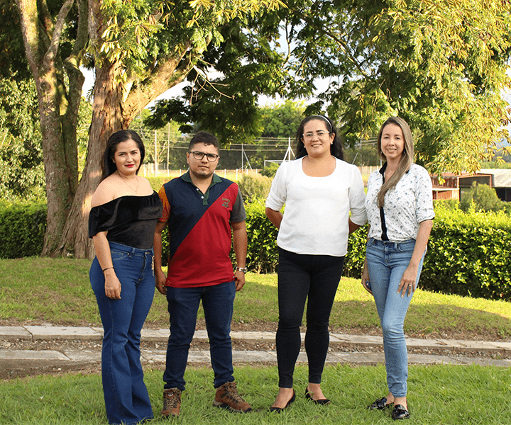 Estudiantes del Eje Cafetero vivieron una experiencia internacional. Fondo verde, con arboles y pantas, tres estudiantes y una docentes, se abrazan de pie y miran al frente.