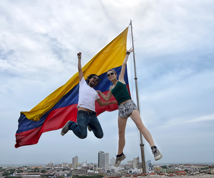 UNIMINUTO fortalece la cultura de “No violencia” en los jóvenes del país Jovenes saltando frente a una bandera de Colombia
