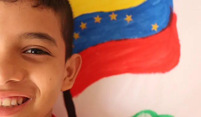 Niño migrante con fondo de la bandera de Venezuela.