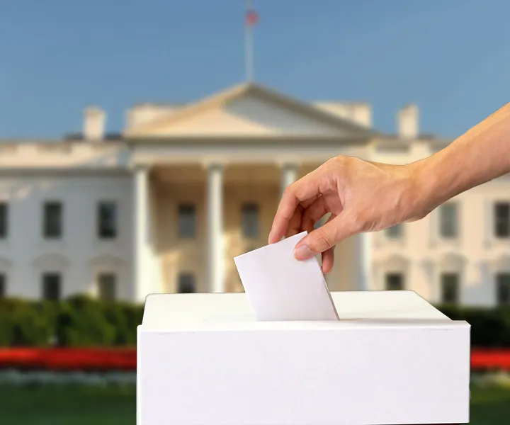 Mano depositando su tarjetón electoral frente a la casa blanca. 