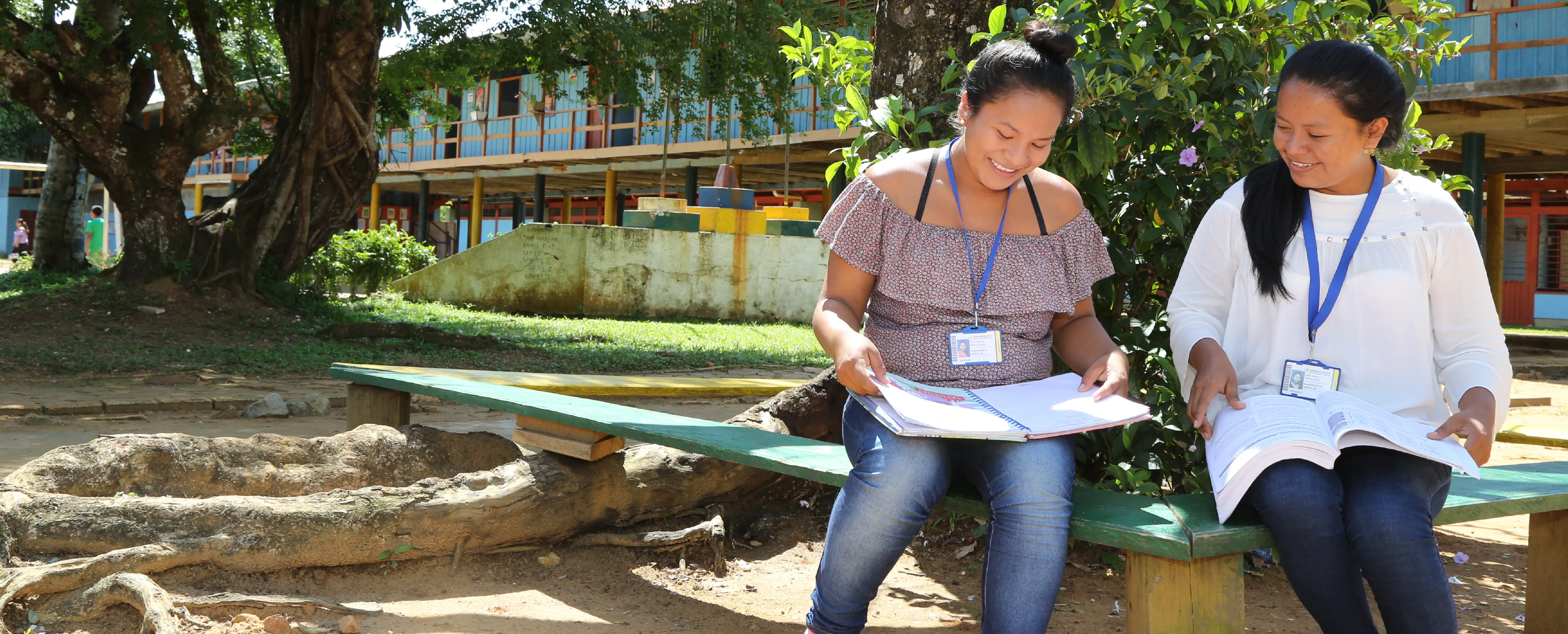 Juntos creamos oportunidades - dos mujeres sentadas en un banco revisando un documento y sonriendo