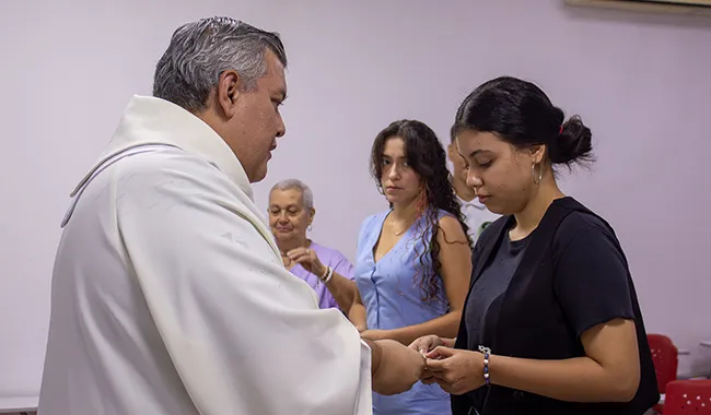 El capellán entrega el pin institucional Cruz Minuto de Dios a una estudiante de Trabajo Social durante la ceremonia de envío.