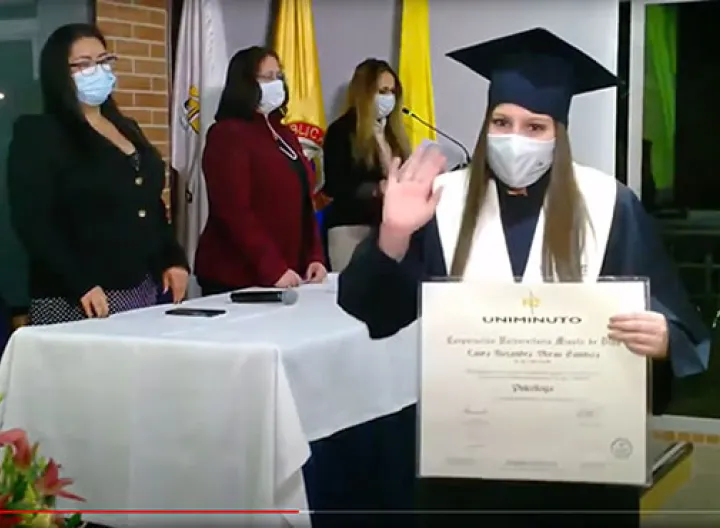 Graduada UNIMINUTO recibe su diploma con toga, birrete y tapabocas. 