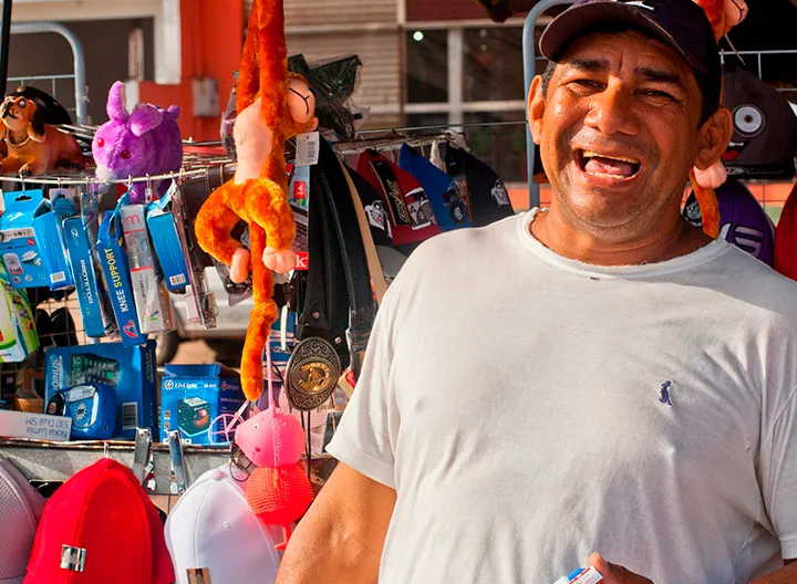 Vendedor informal sonriendo, al fondo se ve su puesto de trabajo con los productos.