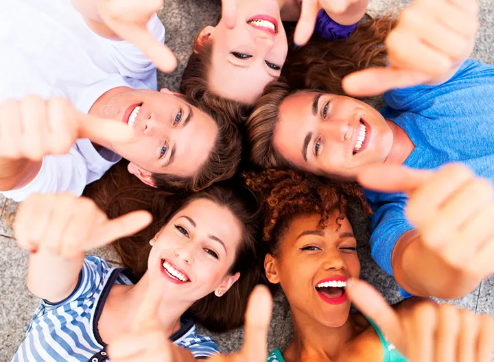 Jóvenes acostados en círculo sonriendo  y haciendo la seña de bien (pulgar arriba)