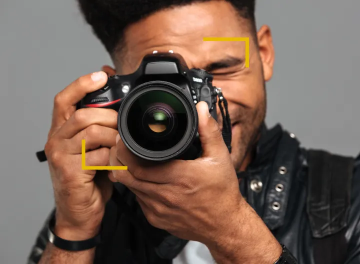 Joven sosteniendo una cámara de fotografía profesional sobre su rostro. 