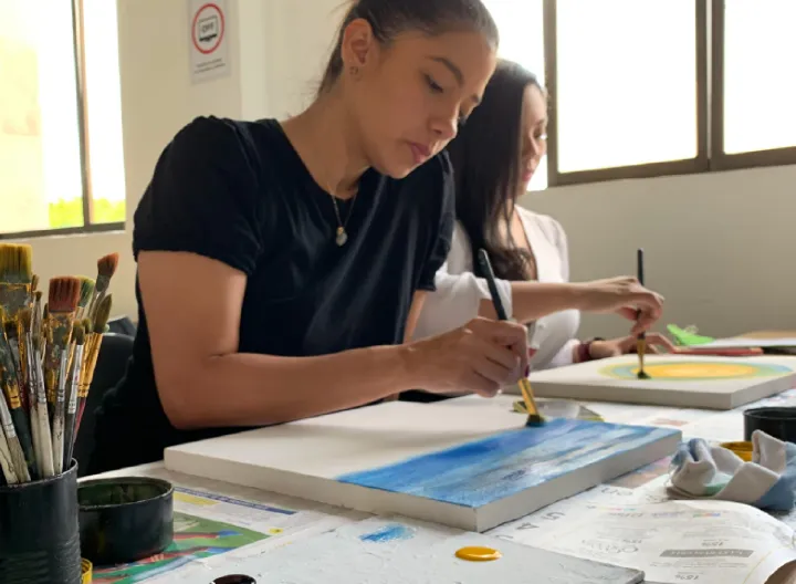 Estudiantes mujeres pintando en un lienzo.