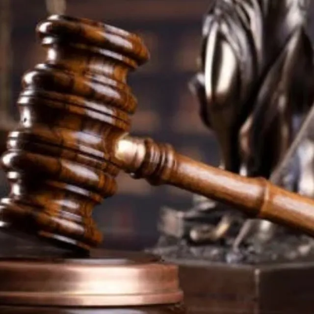 Balanza de la justicia junto a un mazo de juez sobre una mesa, con un reloj de arena y libros de derecho al fondo, representando el concepto de ley, justicia y paso del tiempo en los procesos legales.